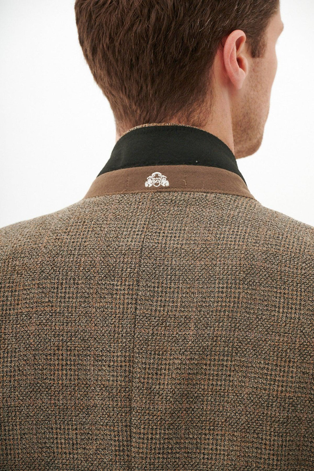 A person is seen from behind wearing the marcdarcy KRIS - Tan Tweed Blazer, featuring a Prince of Wales check pattern, contrasting dark collar, and a small white embroidered design at the back of the neck.