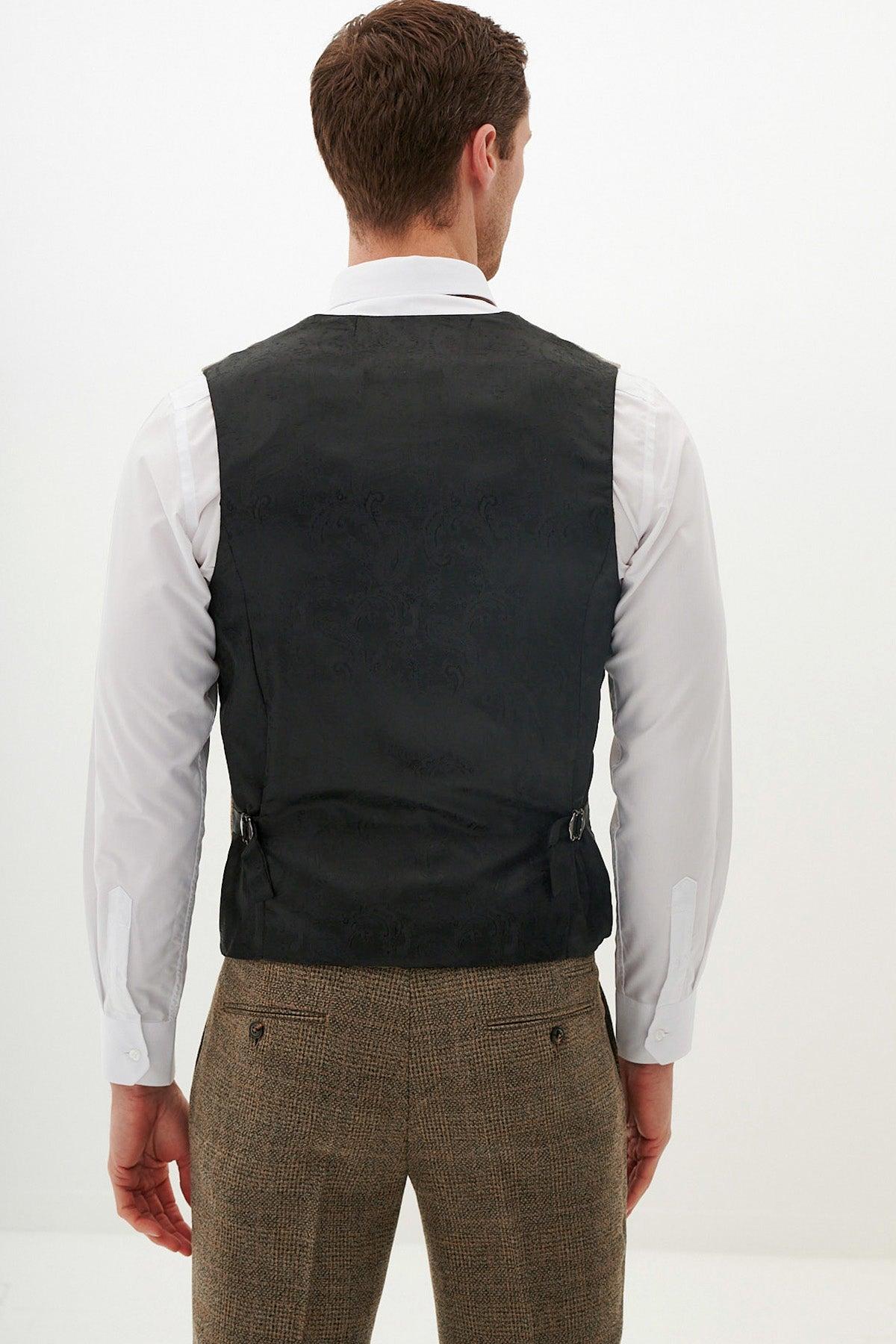 A man faces away, dressed in the marcdarcy KRIS - Tan Tweed Three Piece Suit, featuring a white shirt, black waistcoat with side buckles, and Prince of Wales check trousers, set against a plain white background.