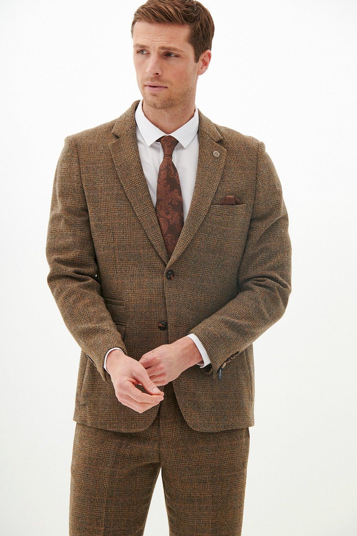 A man wearing the marcdarcy West Bromwich Albion F.C. KRIS Tan Tweed Suit as seen on Jayson Molumby, paired with a white shirt and paisley tie, stands against a white background.