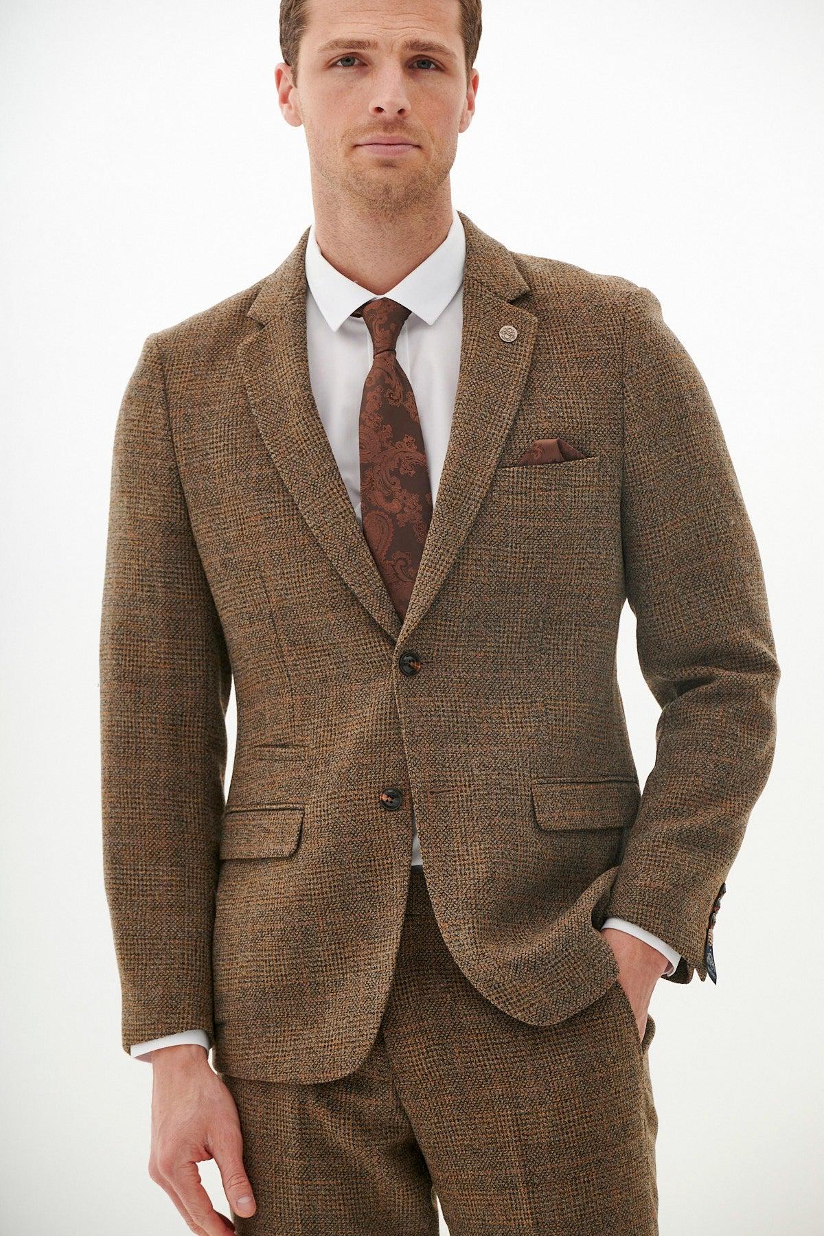 A man in the marcdarcy KRIS Tan Tweed Suit from The West Bromwich Albion F.C. Collection, as seen on Jayson Molumby, paired with a white dress shirt, patterned brown tie, and brown pocket square stands facing forward against a white background.