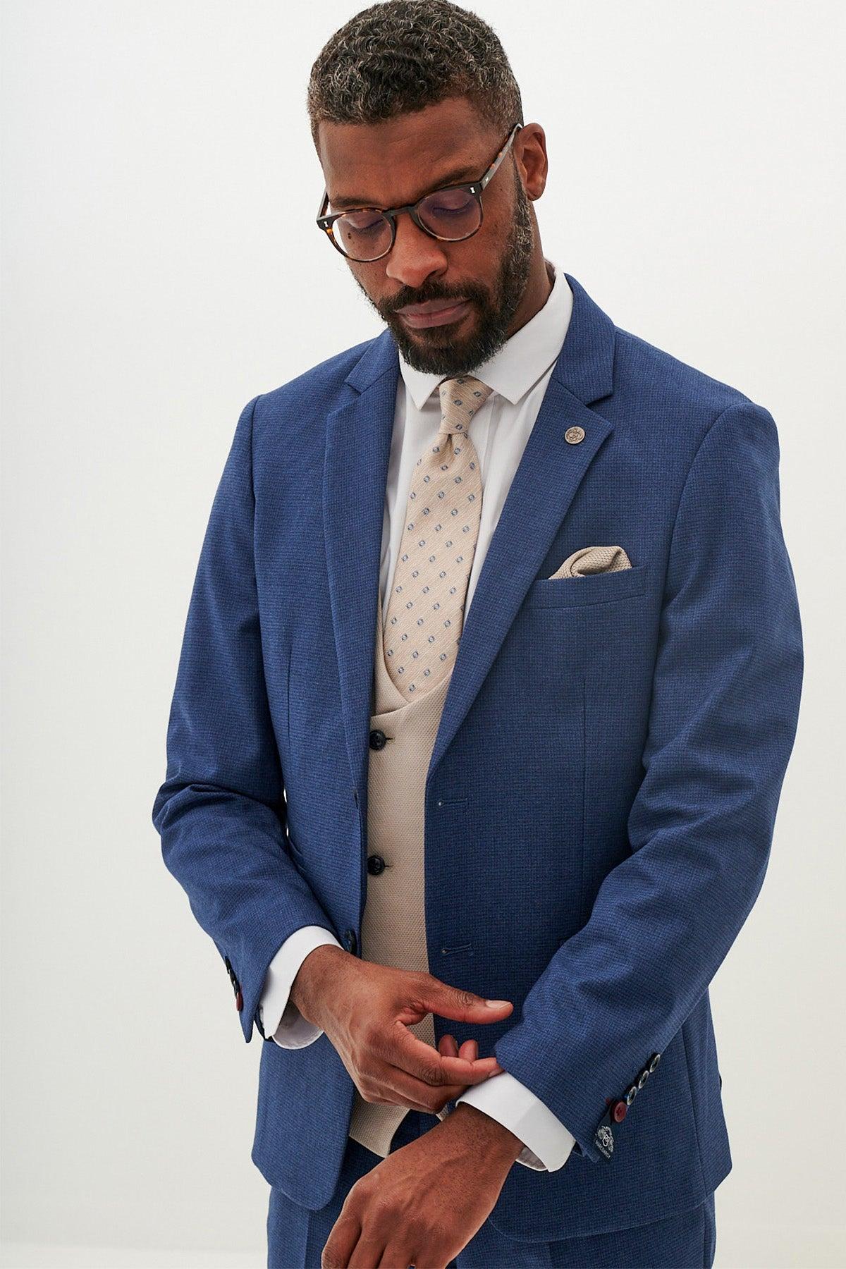 A Black man wearing the Marc Darcy ASHLEY Navy Blue Suit with Kelvin Stone Waistcoat looks down at his hands.