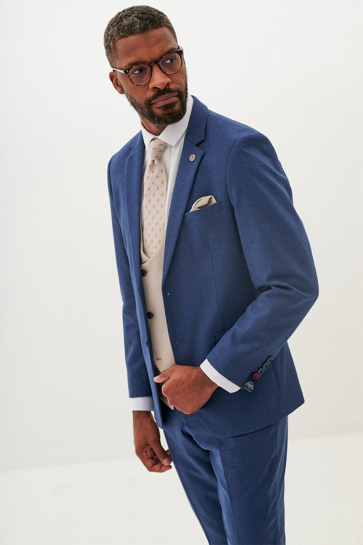 A bearded man in glasses looks to his right, wearing the Marc Darcy ASHLEY navy blue suit with a Kelvin Stone waistcoat and patterned tie.