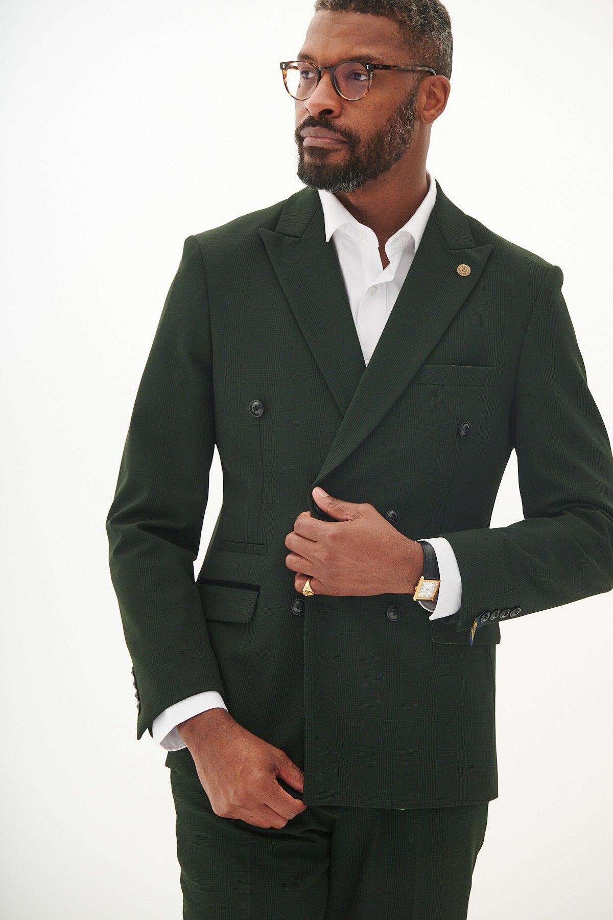 A man with short hair, a beard, and glasses wears the Marc Darcy BROMLEY Olive Green Double Breasted Check Blazer over a white shirt. He stands against a plain light background, adjusting his blazer with one hand.