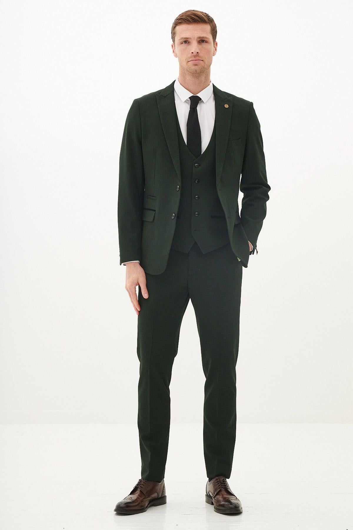 A man stands in the Marc Darcy BROMLEY Olive Green Check Suit from The Leicester City F.C. Collection, as worn by Harry Winks, styled with a crisp white shirt, black tie, and brown dress shoes.