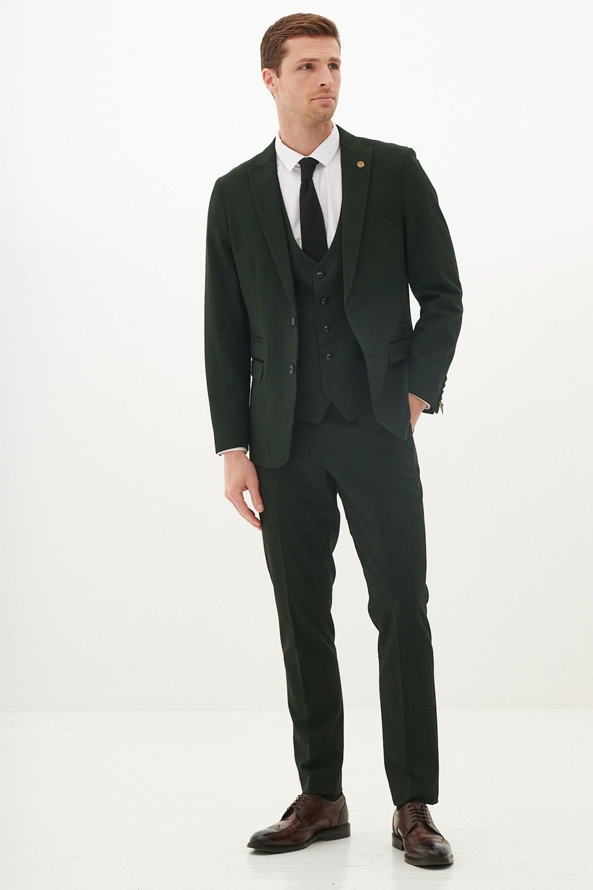 A man models the Marc Darcy BROMLEY Olive Green Check Suit from The Cardiff City F.C. Collection, as worn by Karlan Grant, paired with a white shirt and black tie, standing against a plain white background with hands relaxed by his sides.