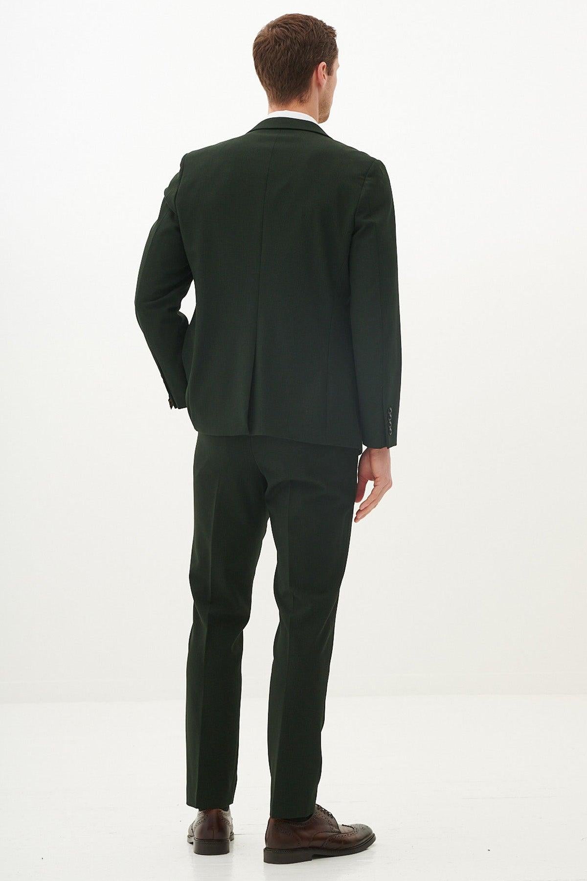 A man faces away from the camera wearing the Marc Darcy BROMLEY Olive Green Check Suit with Kris Tan Tweed Waistcoat, paired with brown dress shoes, against a plain white background.