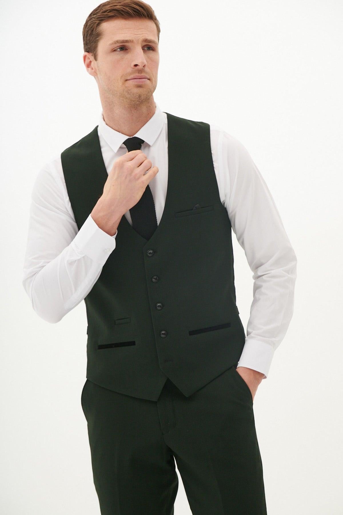 A man wears the Marc Darcy Cardiff City F.C. Collection - BROMLEY Olive Green Check Suit as worn by Karlan Grant, standing against a white background, adjusting his black tie over a crisp white shirt with one hand in his pocket.
