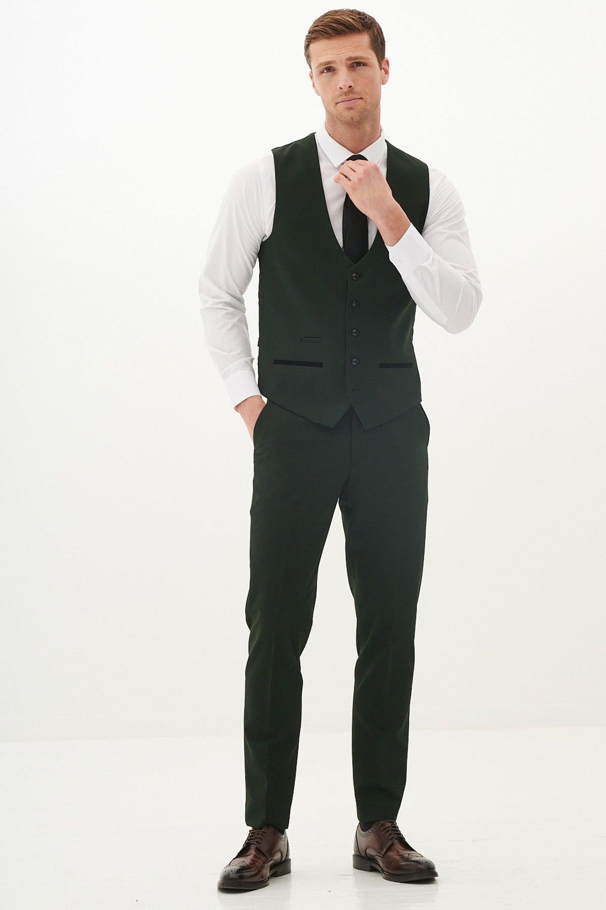 A man wears the Marc Darcy BROMLEY Olive Green Single Breasted Check Waistcoat with a white shirt, black tie, and trousers. He stands with one hand in his pocket while adjusting his tie.