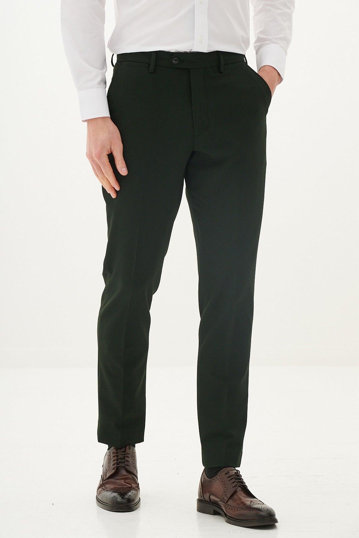 A man stands against a white background wearing the Marc Darcy BROMLEY Olive Green Check Suit with Kris Tan Tweed Waistcoat, paired with a white dress shirt and brown shoes, one hand in his pocket.