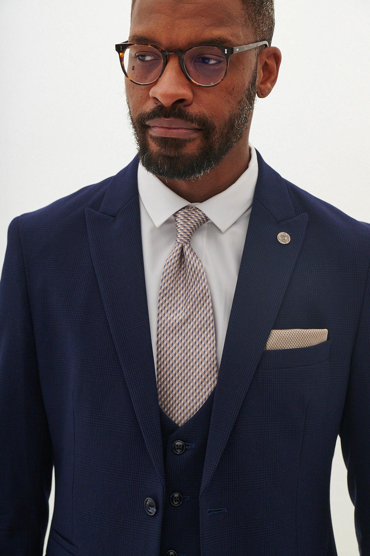 A man wearing the Marc Darcy BROMLEY Navy Three Piece Suit—As Worn By Jarrod Bowen—with a white shirt, patterned tie, and glasses.