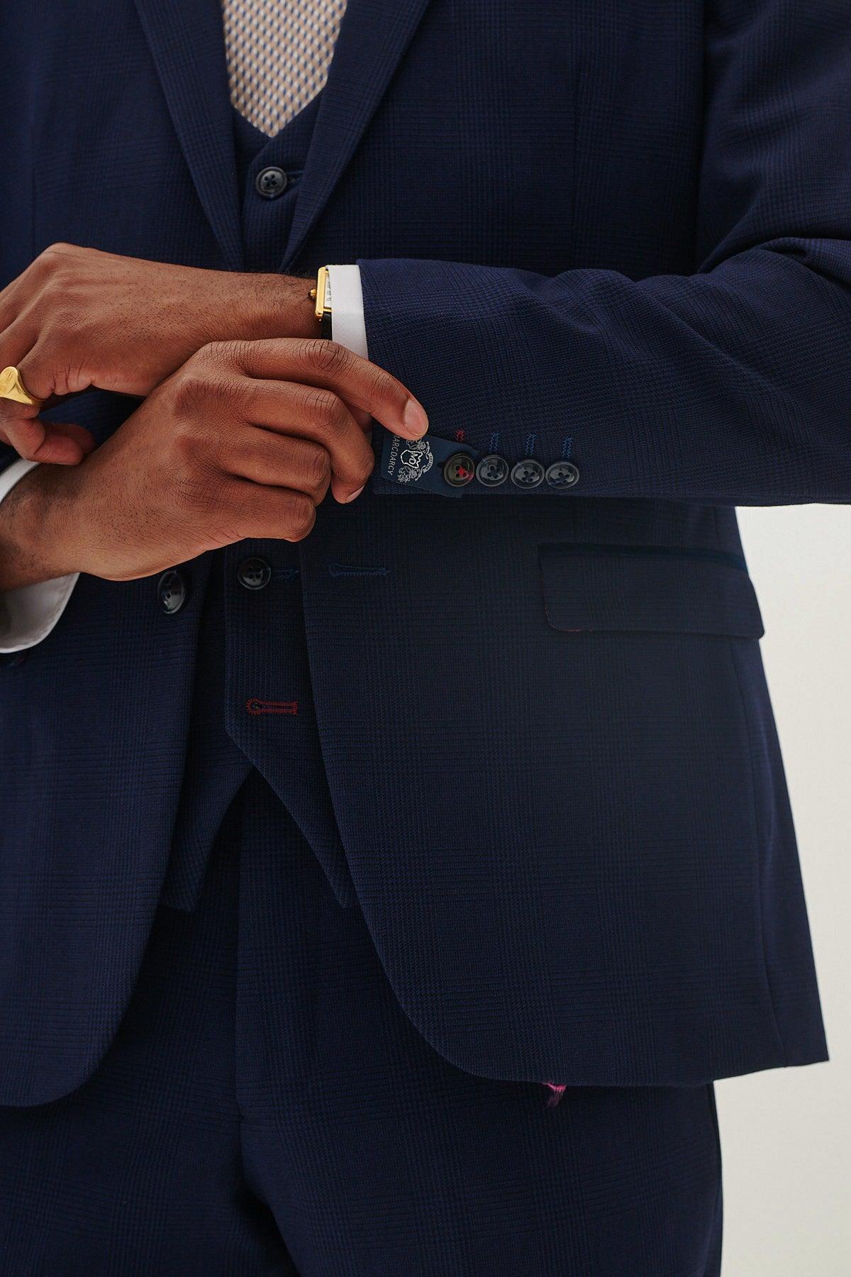 A person wearing the Marc Darcy BROMLEY - Navy Check Blazer adjusts their cuff, revealing only their torso and arms, along with a gold ring, gold watch, and Prince of Wales check patterned shirt cuffs.