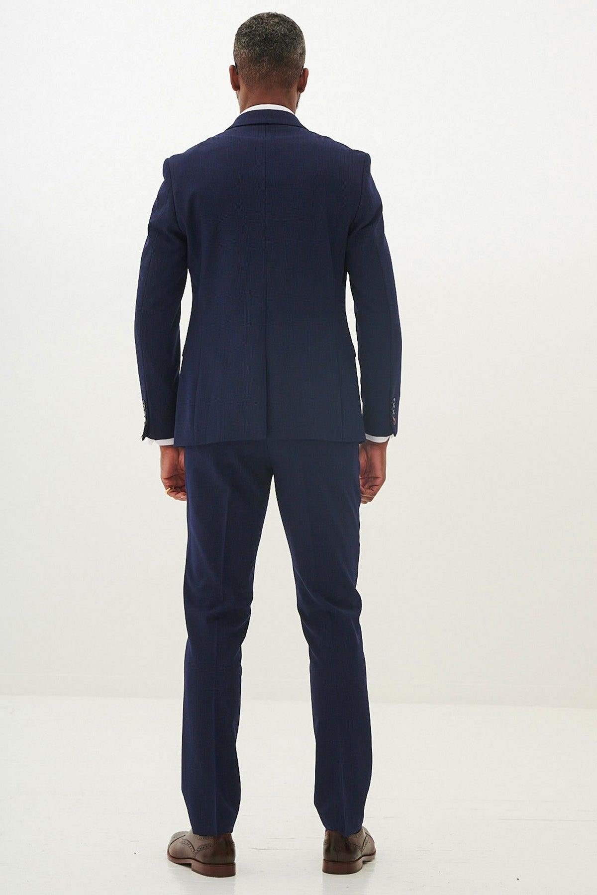 A man stands with his back to the camera wearing the Marc Darcy BROMLEY - Navy Check Blazer, paired with brown dress shoes, against a plain white background.