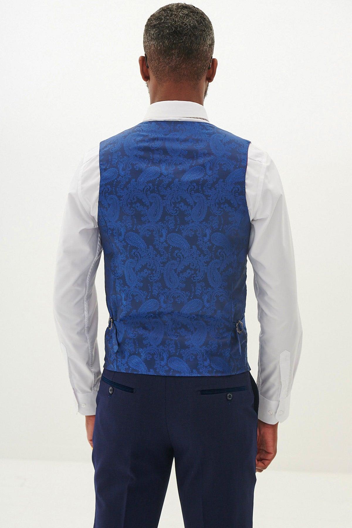 Back view of a man wearing a royal blue paisley jacquard waistcoat over a white shirt and navy trousers from the Marc Darcy BROMLEY Navy Three Piece Suit—an elegant look as worn by Mads Hermansen, featuring an adjustable waistcoat back strap.