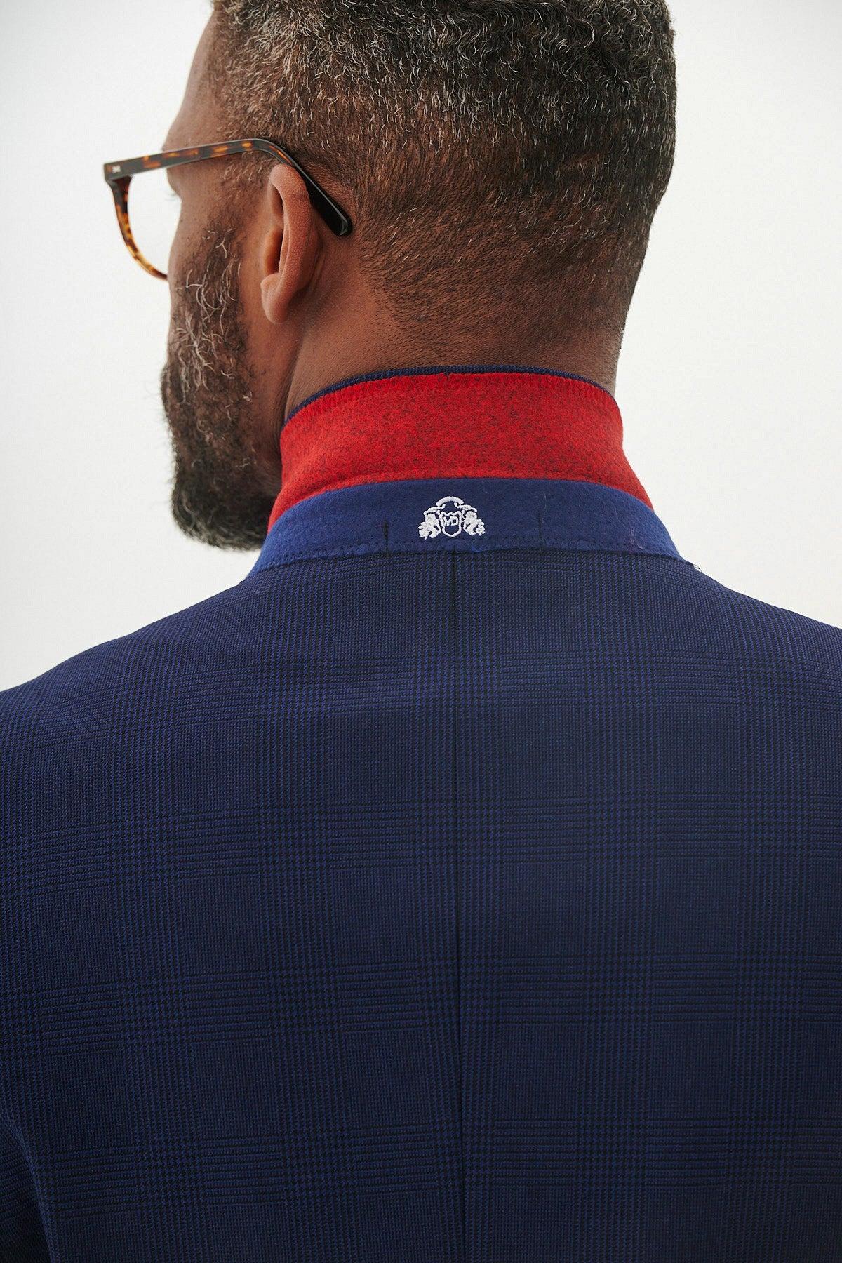 Close-up of a man's neck wearing the Marc Darcy BROMLEY Navy Check Blazer in slim fit, layered over a red turtleneck. The jacket collar features a visible white emblem.