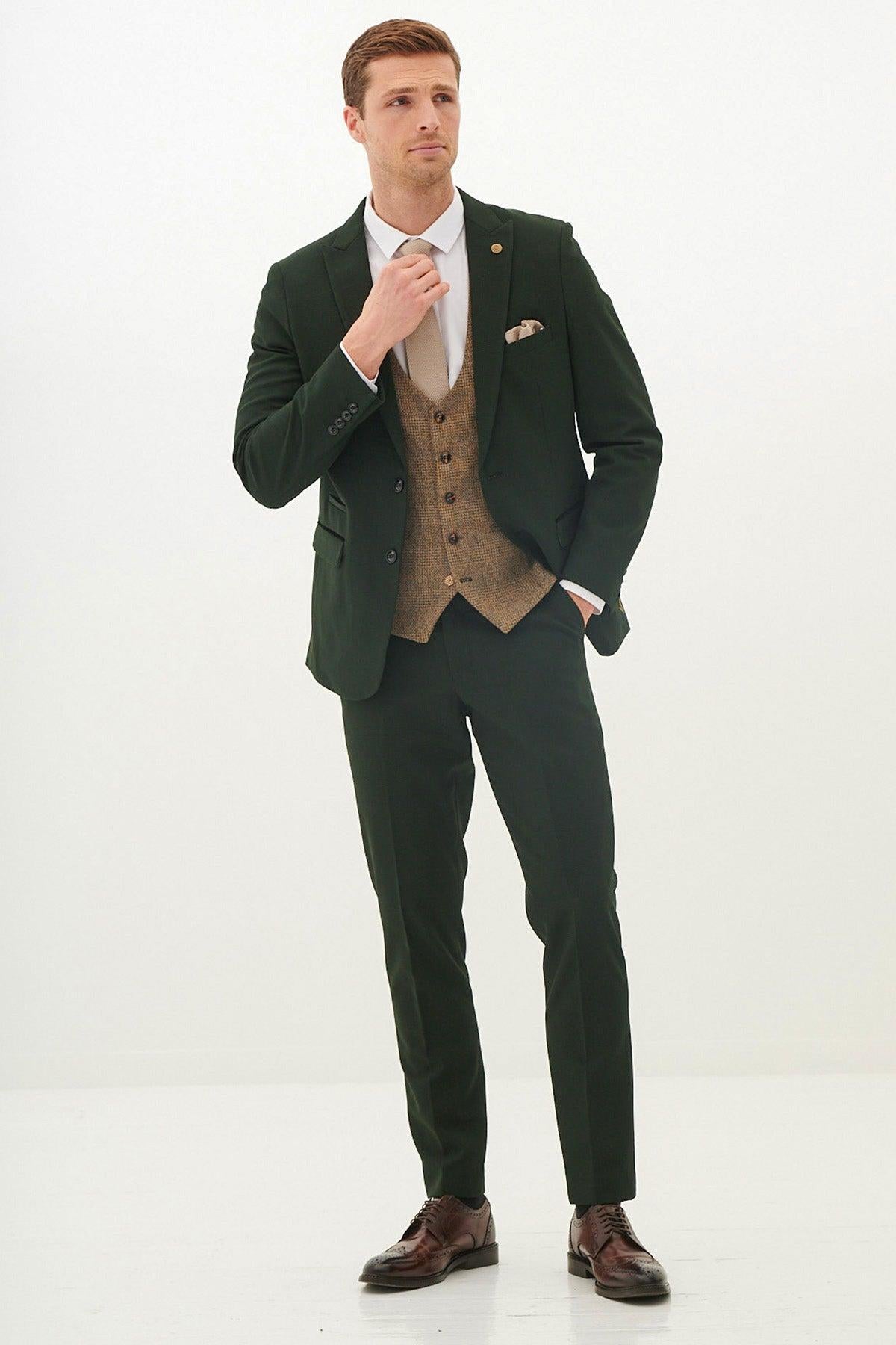 A man in the Marc Darcy BROMLEY Olive Green Check Suit with Kris Tan Tweed Waistcoat adjusts his tie, pairing it with a cream shirt and brown dress shoes.