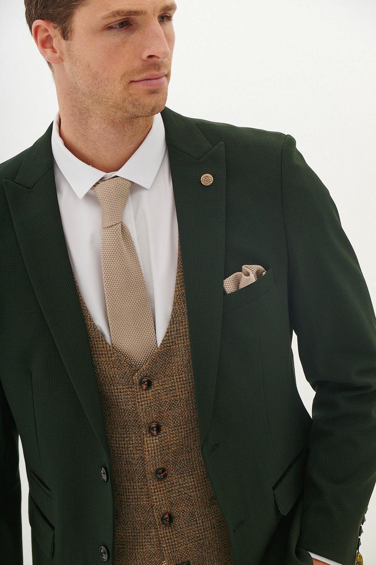 A man wearing the Marc Darcy BROMLEY Olive Green Check Suit with Kris Tan Tweed Waistcoat, a white shirt, beige tie, and pocket square stands against a plain white background.