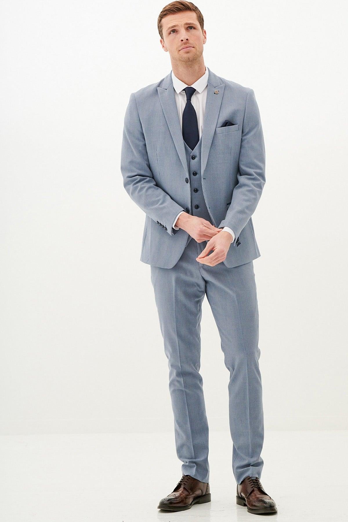A man wearing the Marc Darcy BROMLEY Sky Blue Check Three Piece Suit with a white shirt and dark tie adjusts his cufflinks against a white background.