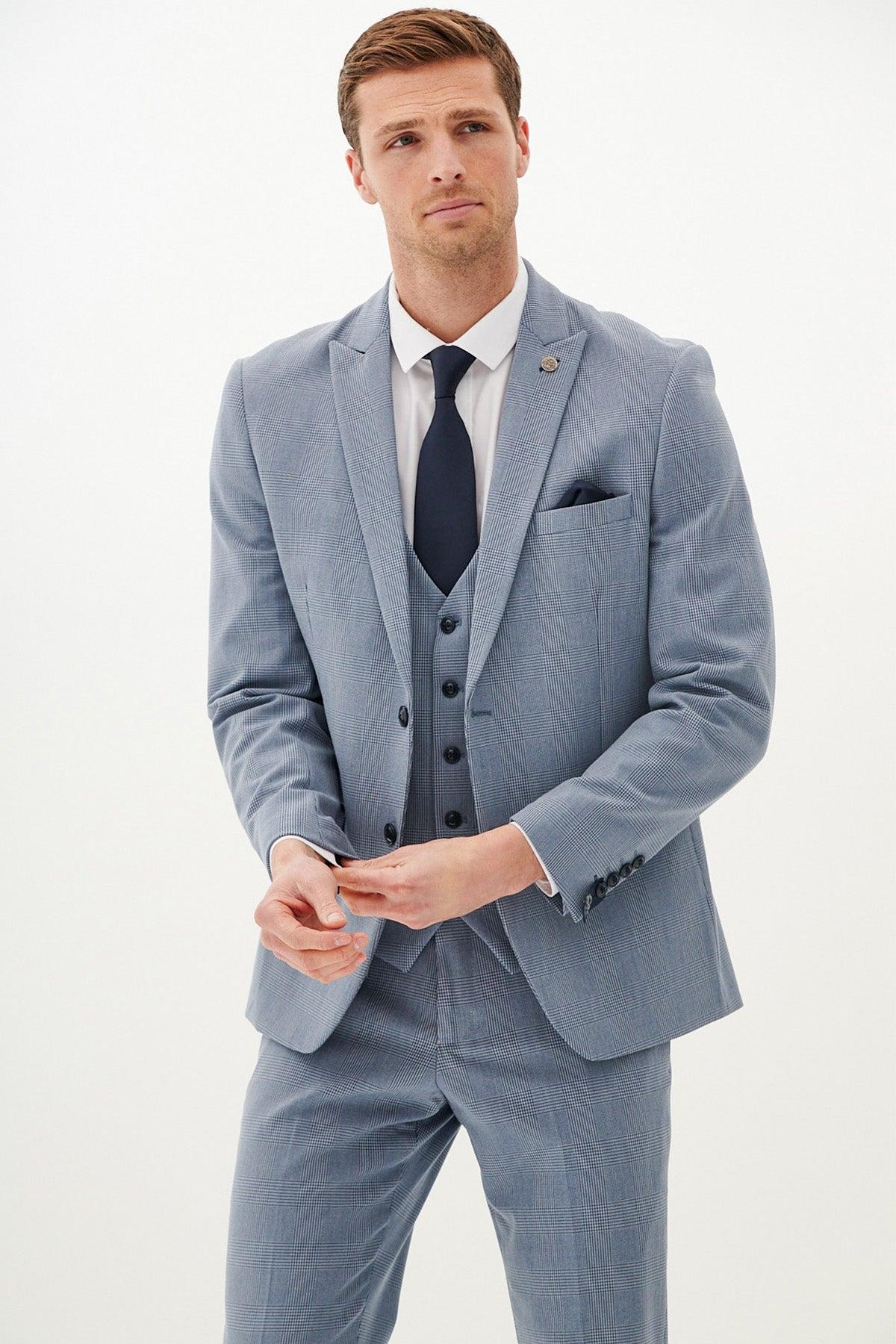A man wearing the Marc Darcy BROMLEY Sky Blue Check Three Piece Suit stands against a plain white background, adjusting his cuff with a serious expression.