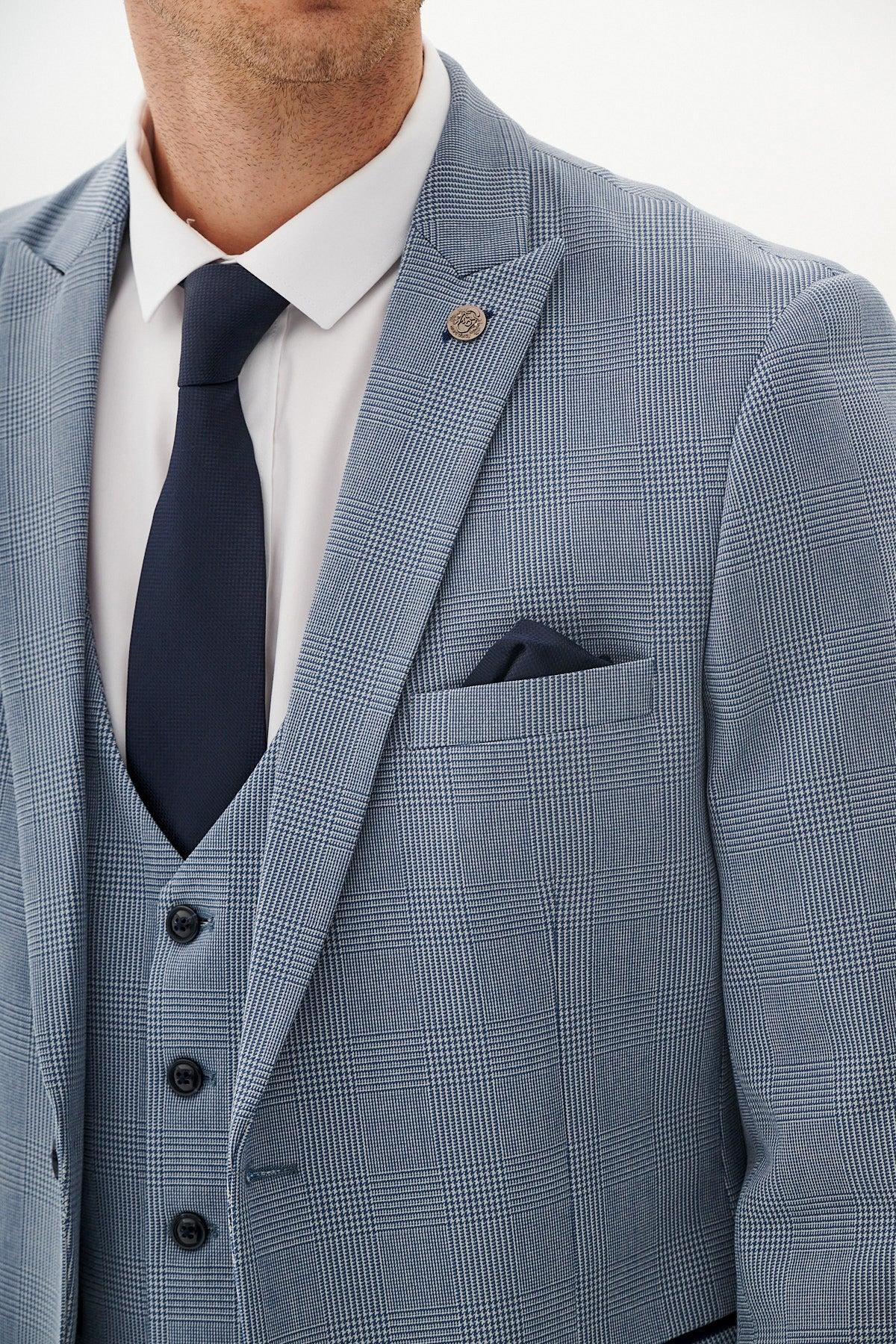A man wears the Marc Darcy BROMLEY - Sky Check Suit with Kelvin Navy Waistcoat, styled with a white shirt, navy tie, matching pocket square, and lapel pin. His head is partially out of frame.