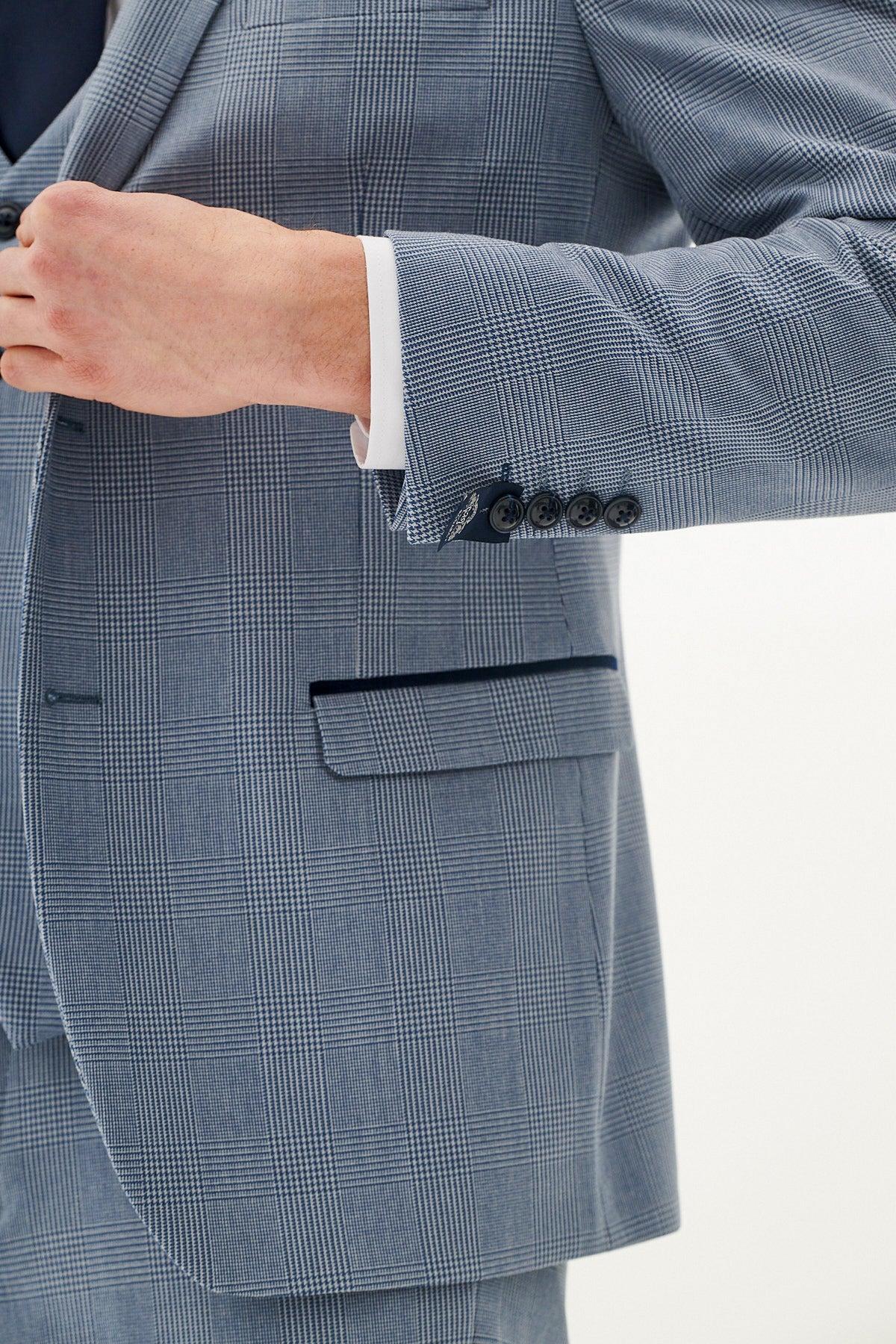 A close-up of a person wearing the Marc Darcy BROMLEY - Sky Check Suit with Kelvin Navy Waistcoat, featuring dark buttons and a white shirt, adjusting the suit against a plain light background.