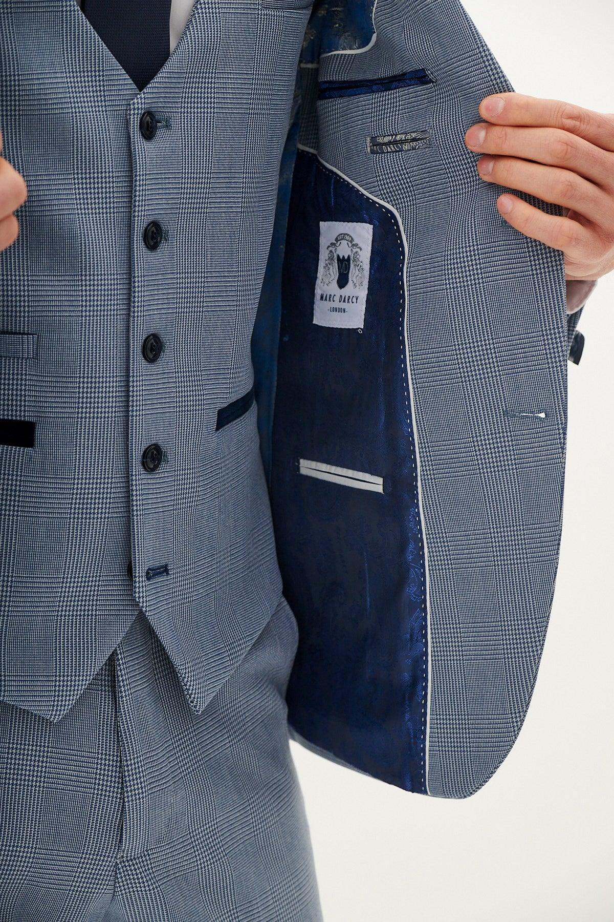 A person wearing the Marc Darcy BROMLEY - Sky Blue Check Blazer holds open the jacket to reveal a dark blue inner lining and a label. The suit features matching vest and pants.