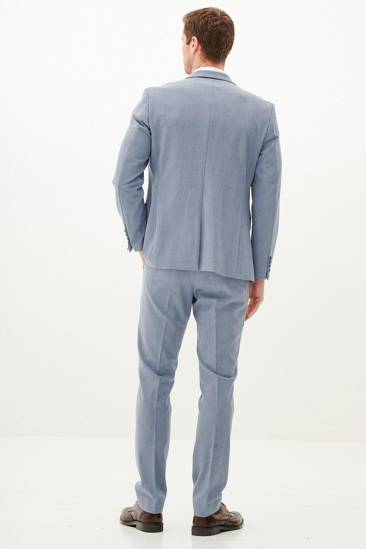A man faces away from the camera wearing the Marc Darcy BROMLEY - Sky Blue Check Three Piece Suit and brown shoes, standing on a light-colored floor with a white background.