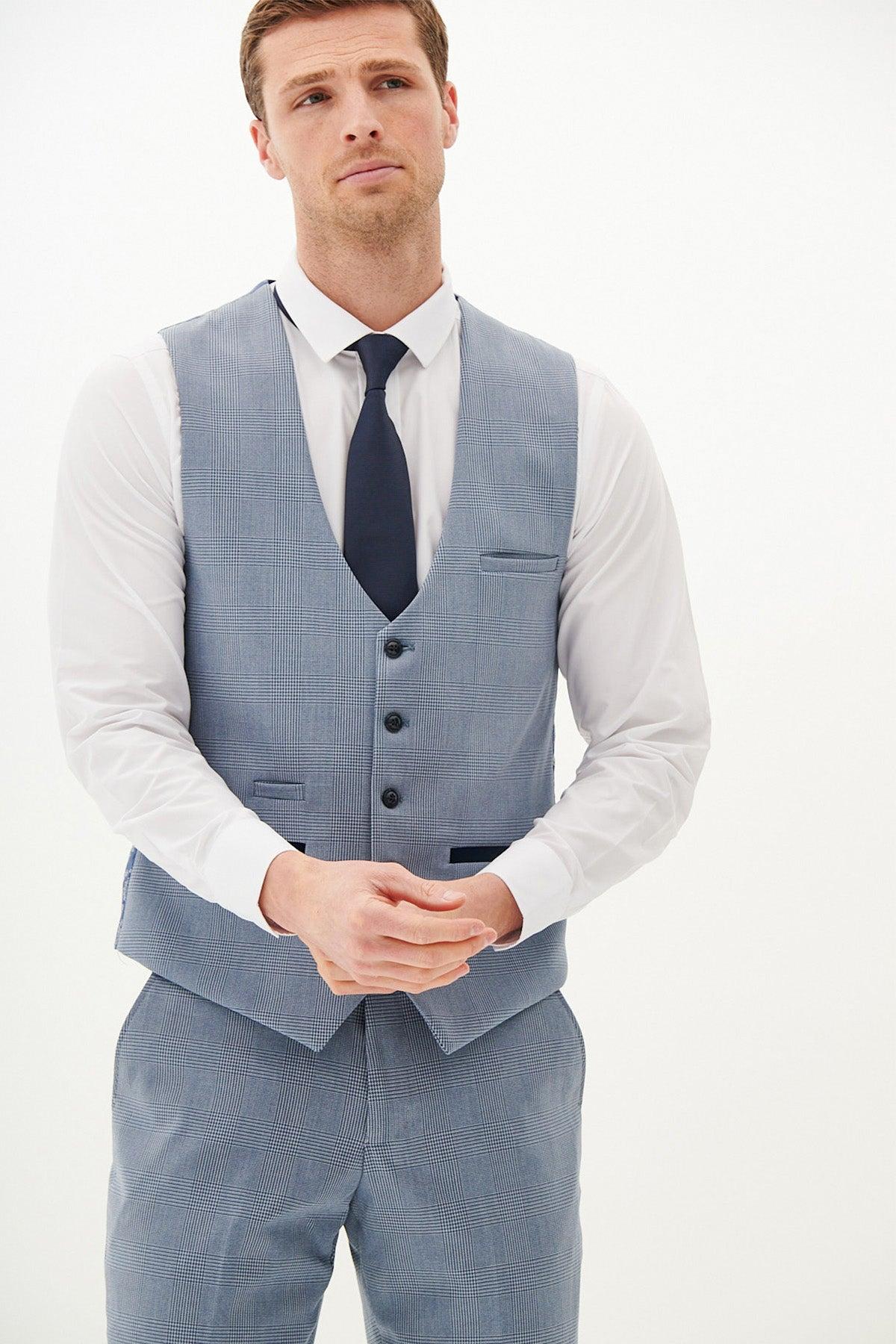 A man wears the Marc Darcy BROMLEY Sky Blue Single Breasted Check Waistcoat with matching pants, a white dress shirt, and dark tie, standing against a plain white background with hands clasped.
