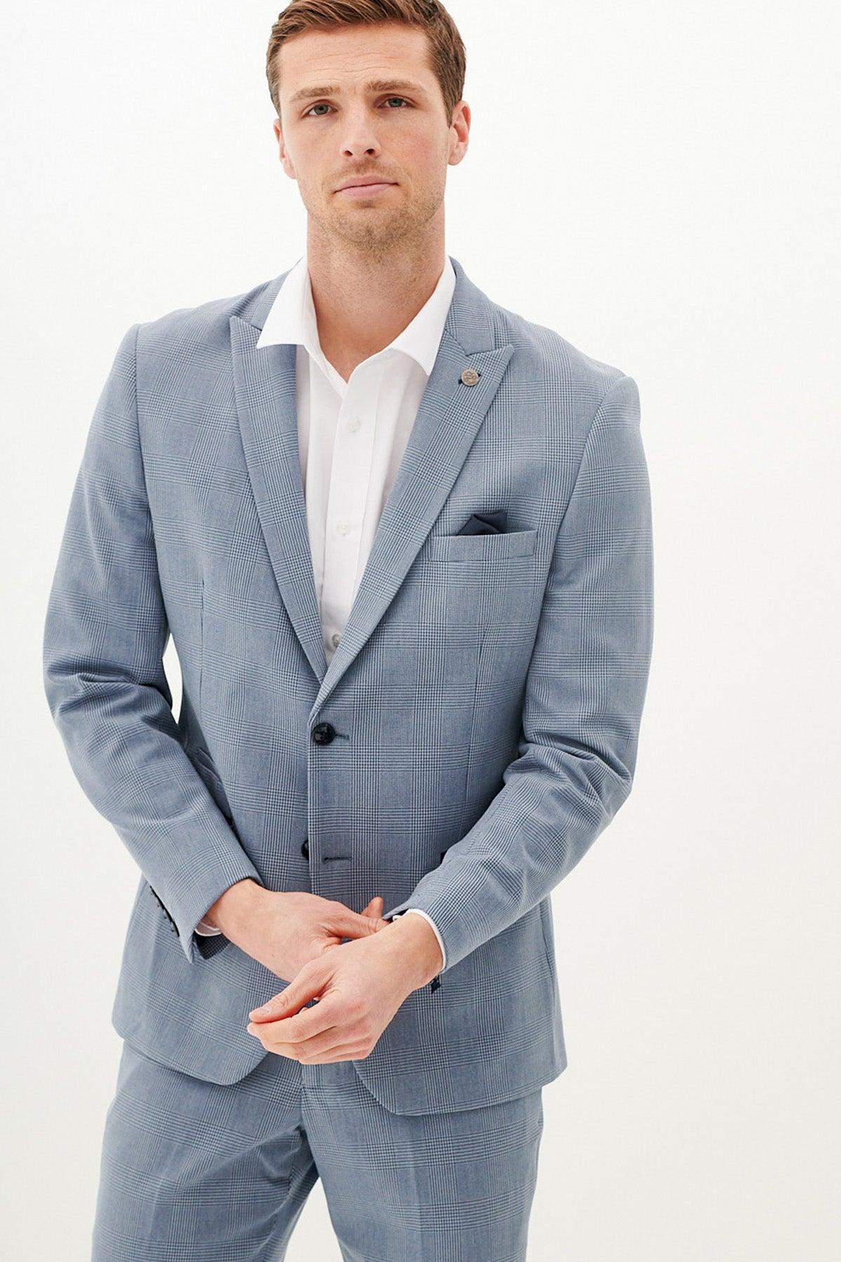 A man wears the Marc Darcy BROMLEY - Sky Blue Check Blazer over a white shirt, standing against a plain white background and looking at the camera with a neutral expression, hands loosely clasped in front.