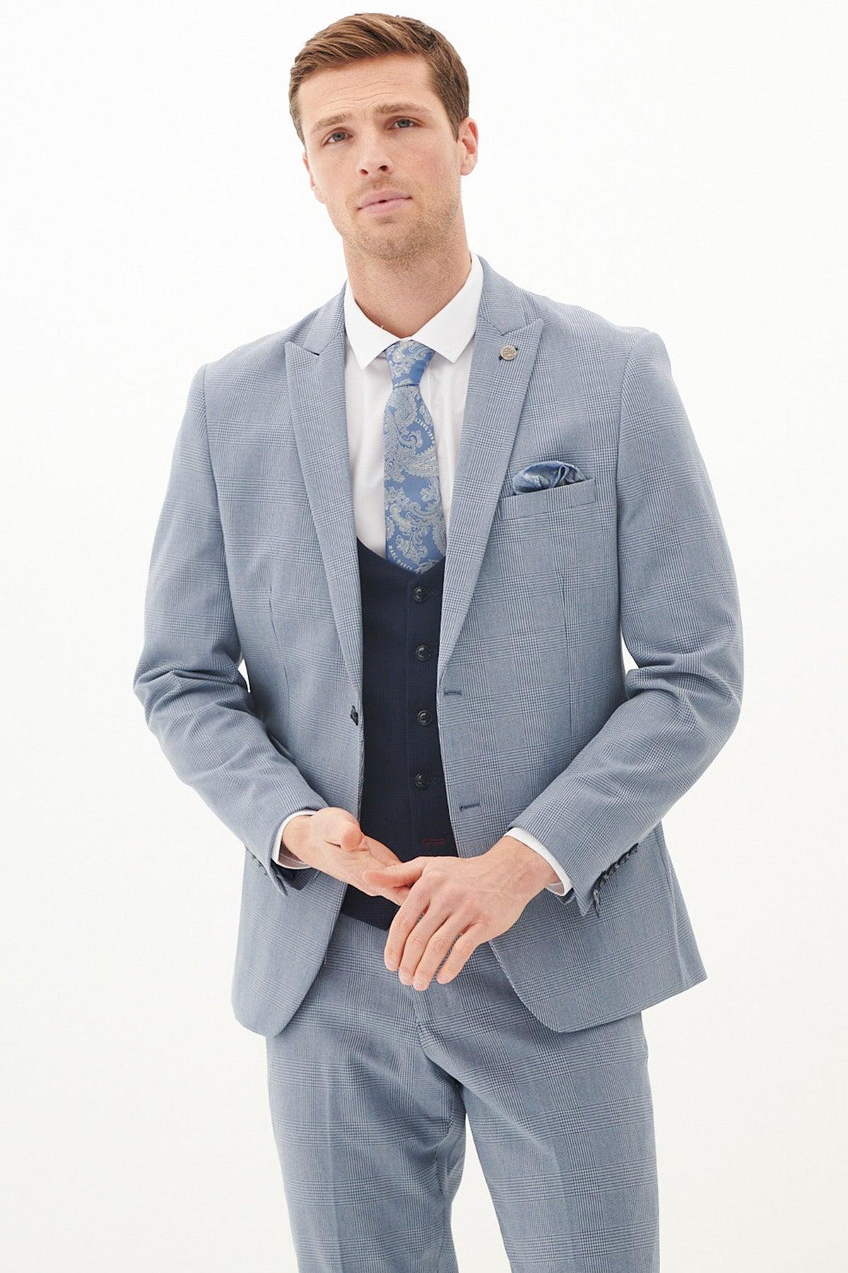 A man wears the Marc Darcy BROMLEY Sky Check Suit with Kelvin Navy Waistcoat, a white shirt, and a patterned blue tie, standing against a white background.