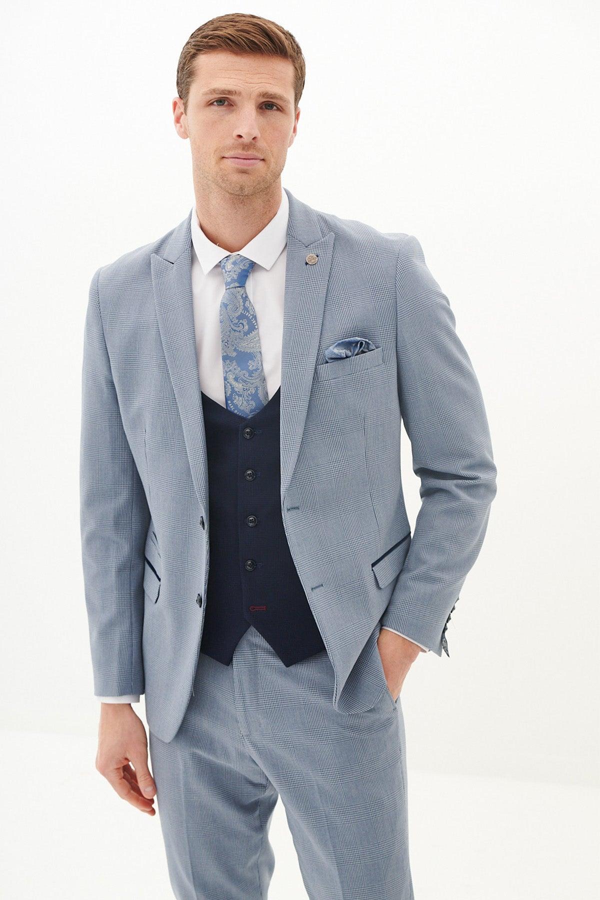 A man with short light brown hair and a neutral expression models the Marc Darcy BROMLEY - Sky Check Suit with Kelvin Navy Waistcoat against a plain white background, styled with a white shirt and patterned blue tie.