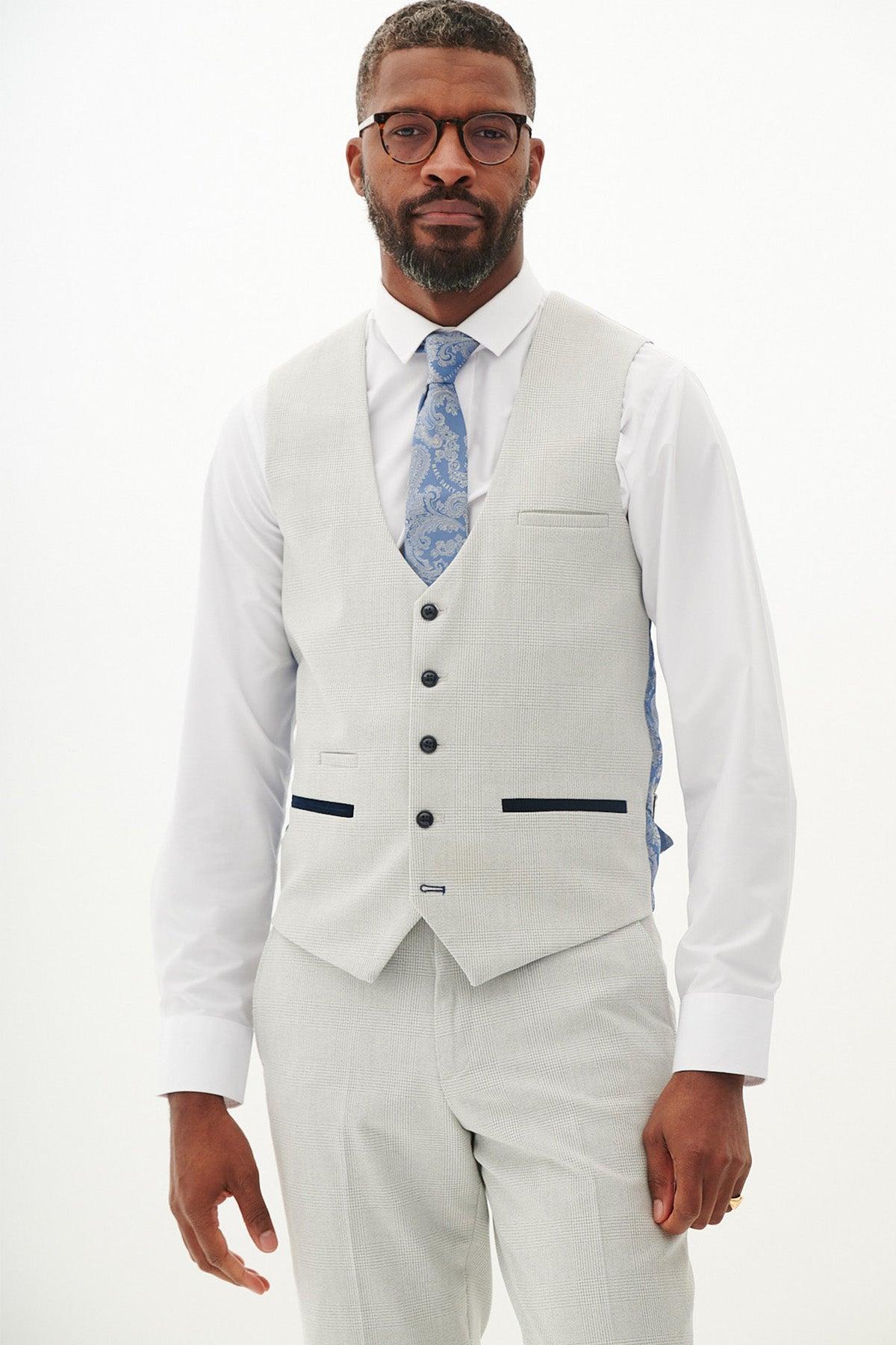 A man with glasses and a beard wears the Marc Darcy BROMLEY stone single breasted check waistcoat, paired with a white shirt and blue patterned tie.