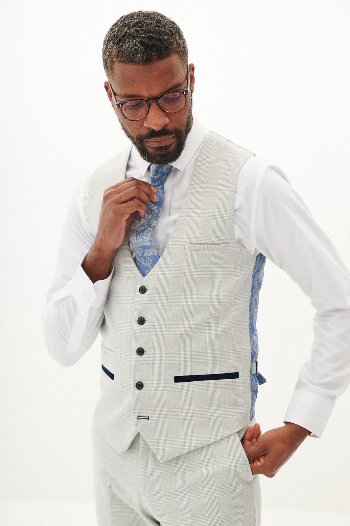 A man in the Marc Darcy BROMLEY Stone Check Three Piece Suit adjusts his blue patterned tie.