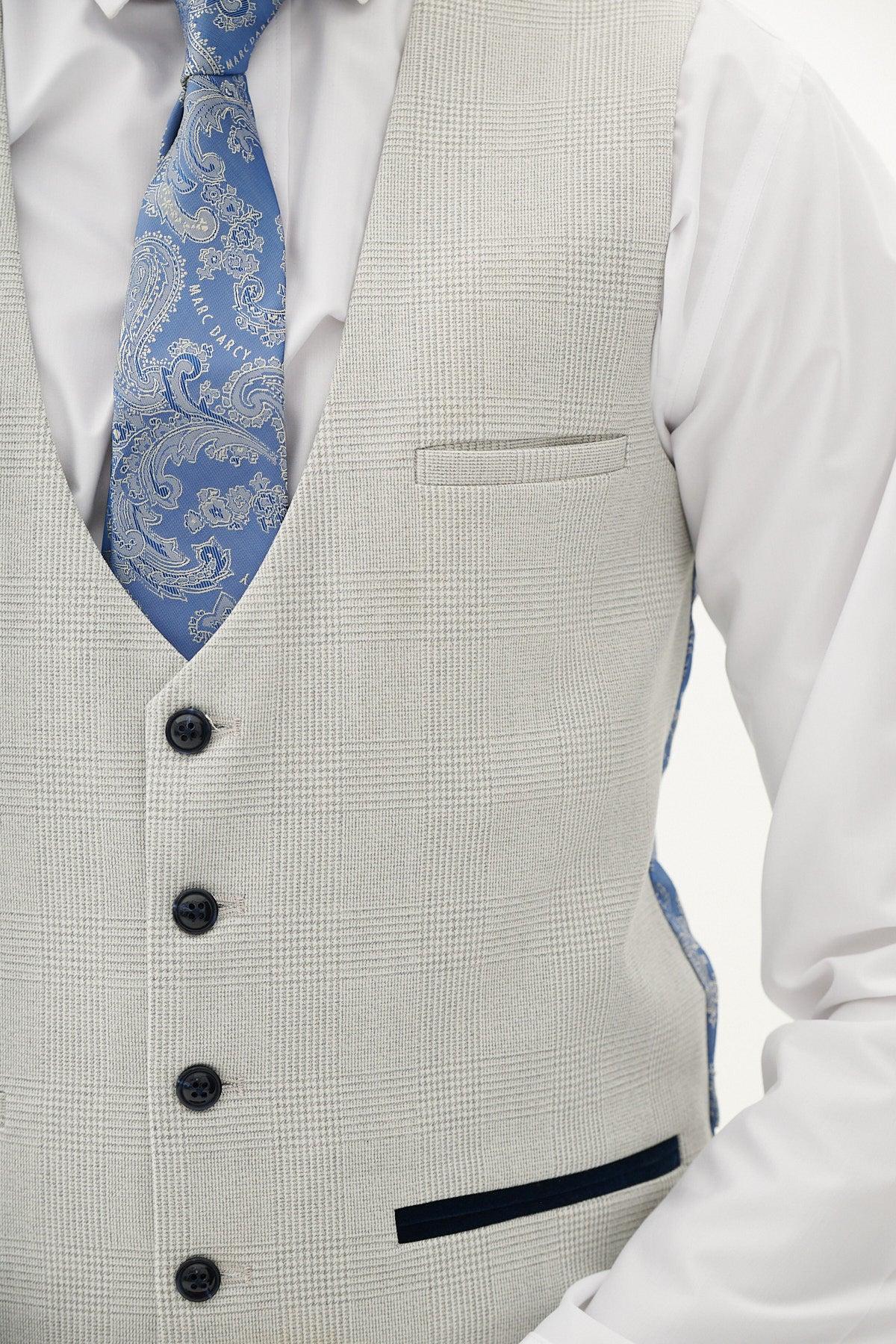 A person wears the Marc Darcy BROMLEY Stone Check Three Piece Suit vest over a white dress shirt and blue paisley tie. The light gray Prince of Wales check vest with black buttons is shown, focusing on the torso of this slim fit look.