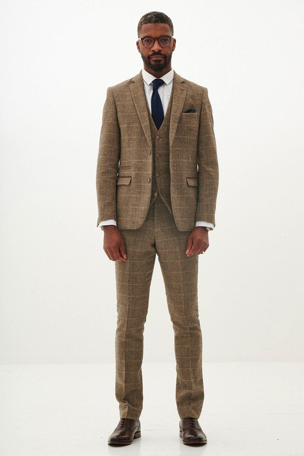 A man faces forward wearing the marcdarcy TED Tan Tweed Check Three Piece Suit with a white shirt, dark blue tie, and brown dress shoes against a plain white background.