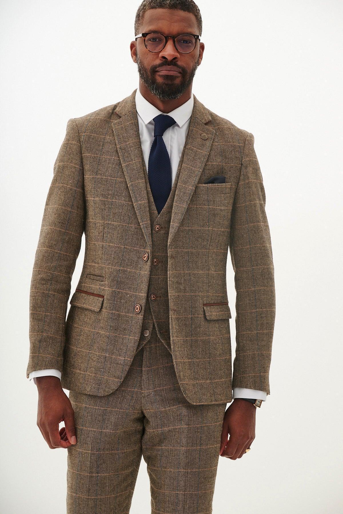 A man in glasses wears a marcdarcy TED Tan Tweed Check Blazer three-piece suit with a white shirt and navy tie, standing against a plain light background.