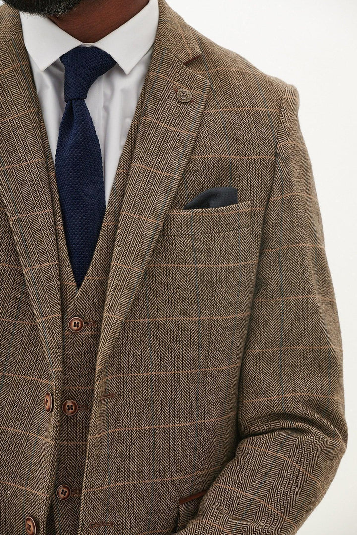 A close-up of a man wearing the marcdarcy TED - Tan Tweed Check Blazer as part of a brown three-piece suit, paired with a white shirt, navy tie, and dark pocket square. His face is partially out of frame.