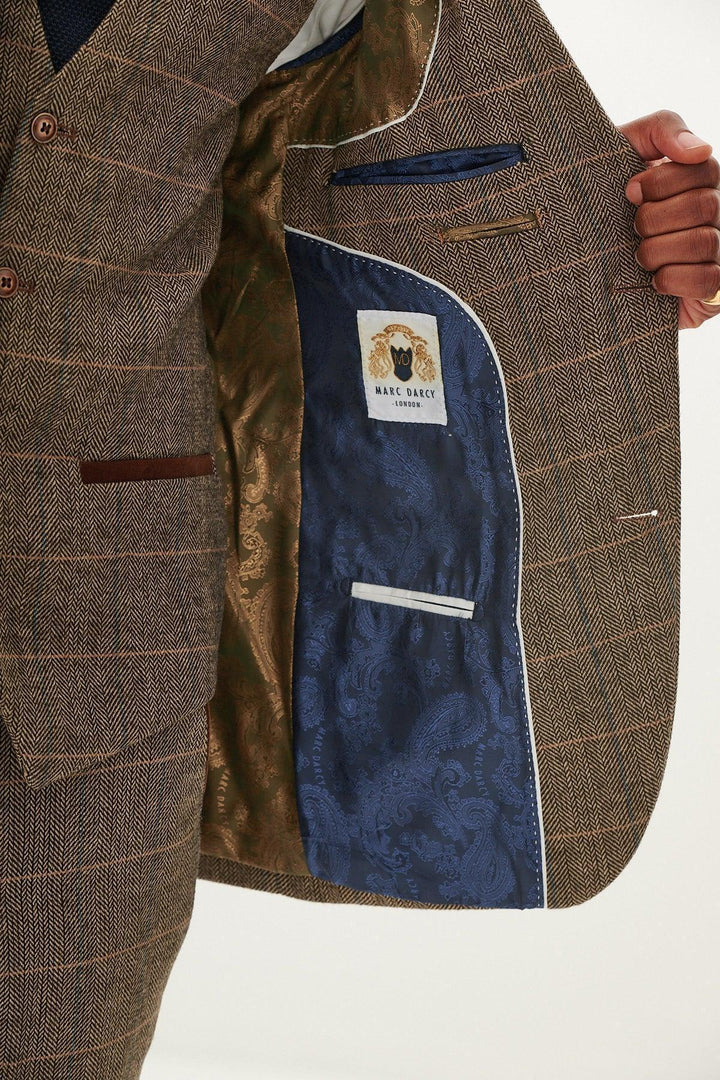 A person holds open the marcdarcy TED - Tan Tweed Check Blazer, showing its inner blue and gold paisley lining, white trim, pockets, and a sewn “marcdarcy” label.