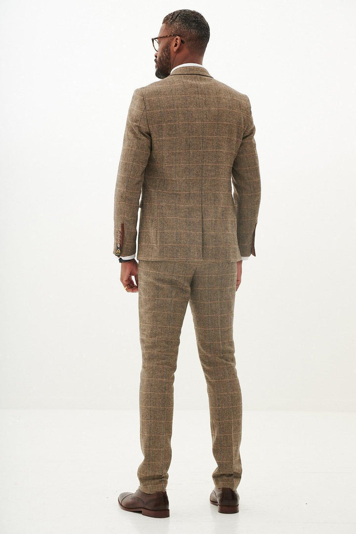 A man stands facing away in a marcdarcy TED - Tan Tweed Check Blazer with matching trousers and brown shoes, in a plain, well-lit studio.