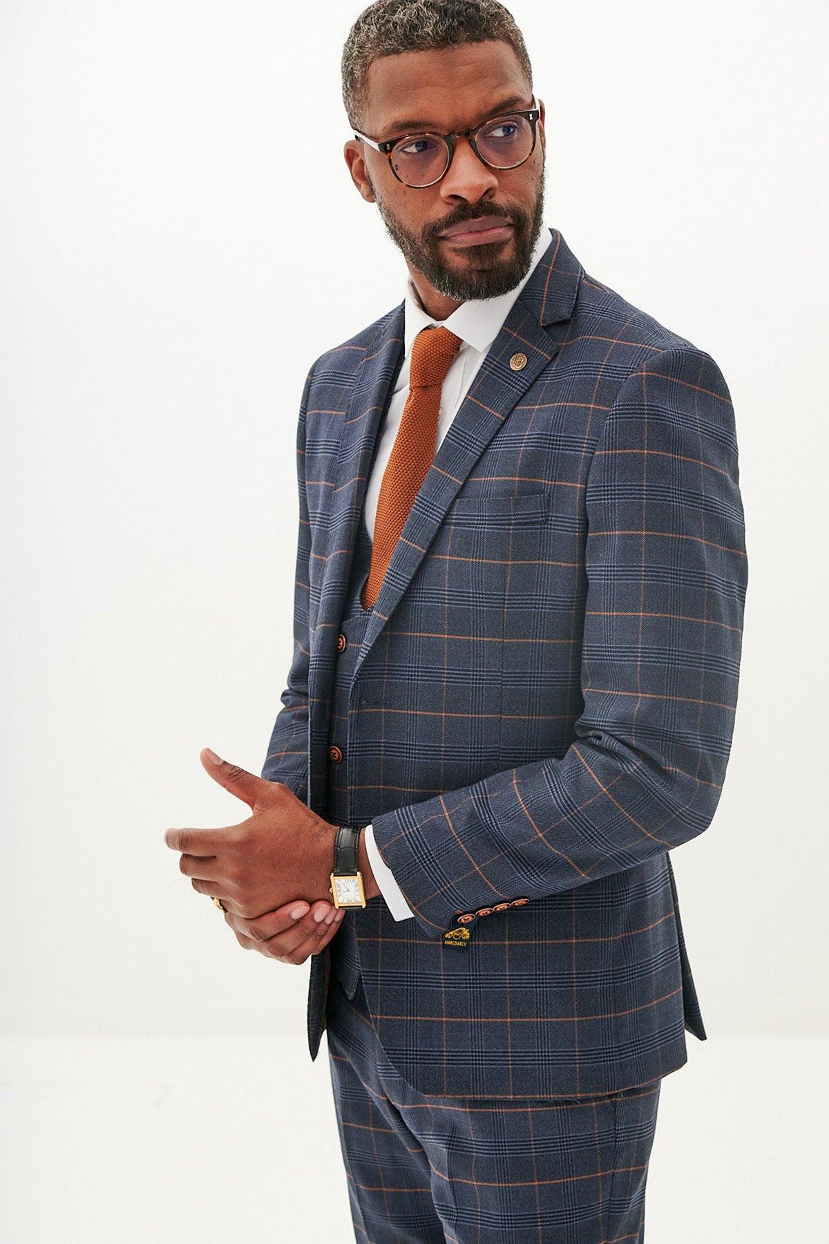 A man with short hair and a beard, wearing glasses, models the marcdarcy JENSON Marine Navy Check Blazer with a white shirt and orange tie, standing against a plain white background and looking to the side.