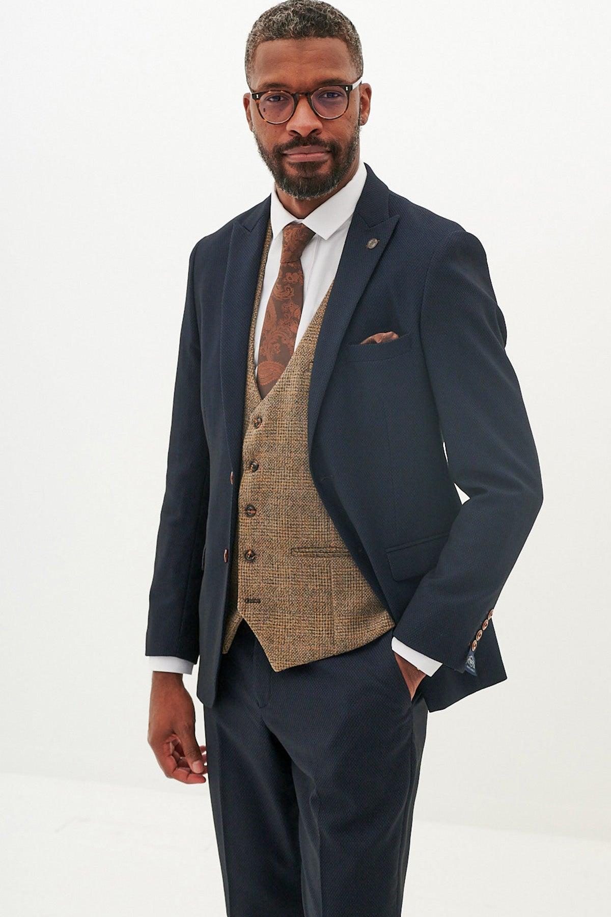 A man with short hair, a beard, and glasses wears the marcdarcy MAX - Navy Suit with Kris Tan Tweed Waistcoat, a white shirt, and a brown tie with matching pocket square against a plain white background.