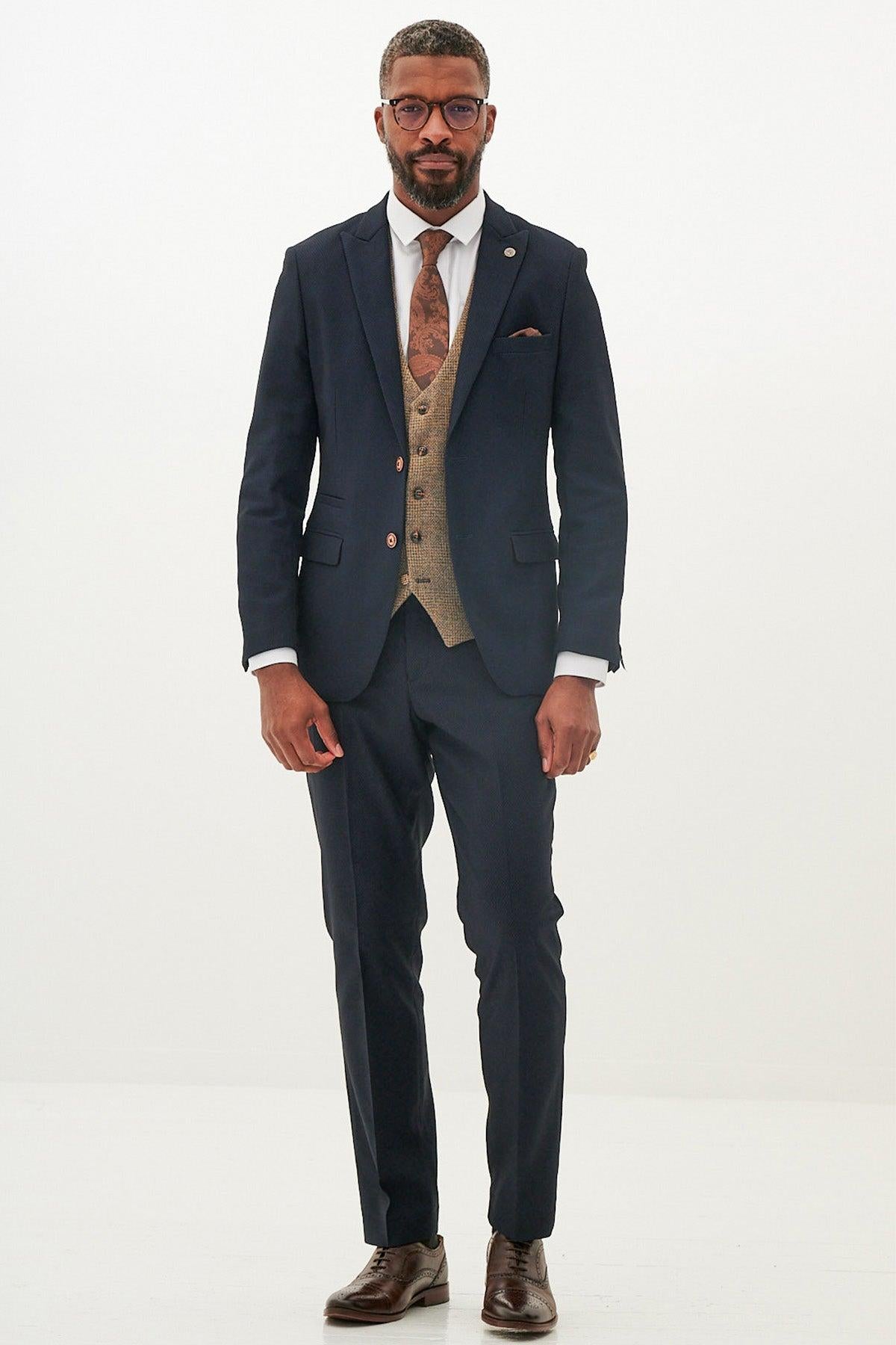 A Black man wears the marcdarcy MAX - Navy Suit with Kris Tan Tweed Waistcoat, paired with a white shirt and brown tie, standing against a white background—a sophisticated formal occasion look.