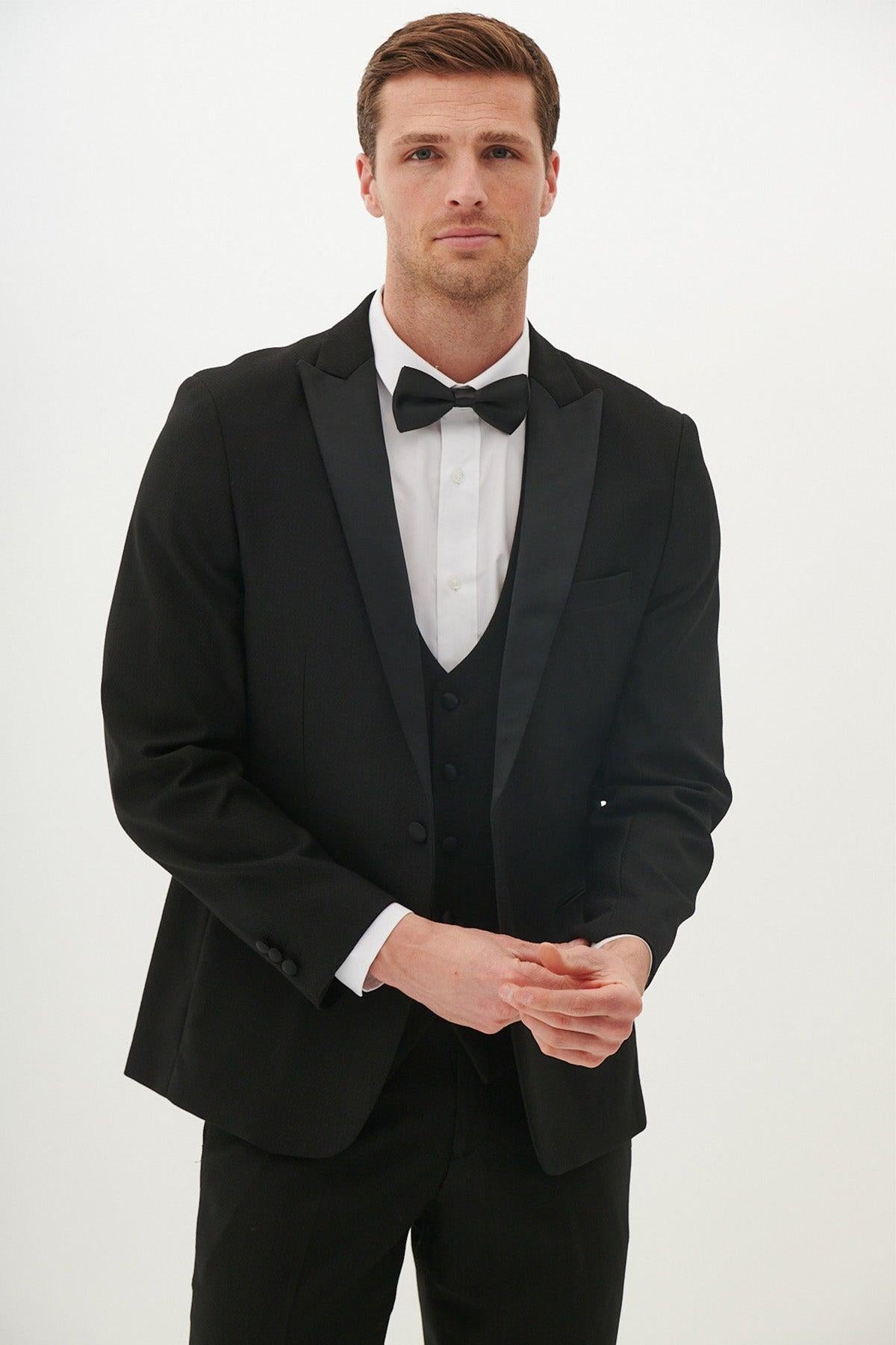 A man wears the marcdarcy Matching Father & Son | DALTON - Black Tux Three Piece Suit with a white shirt and black bow tie, standing against a plain white background and facing the camera with a neutral expression.