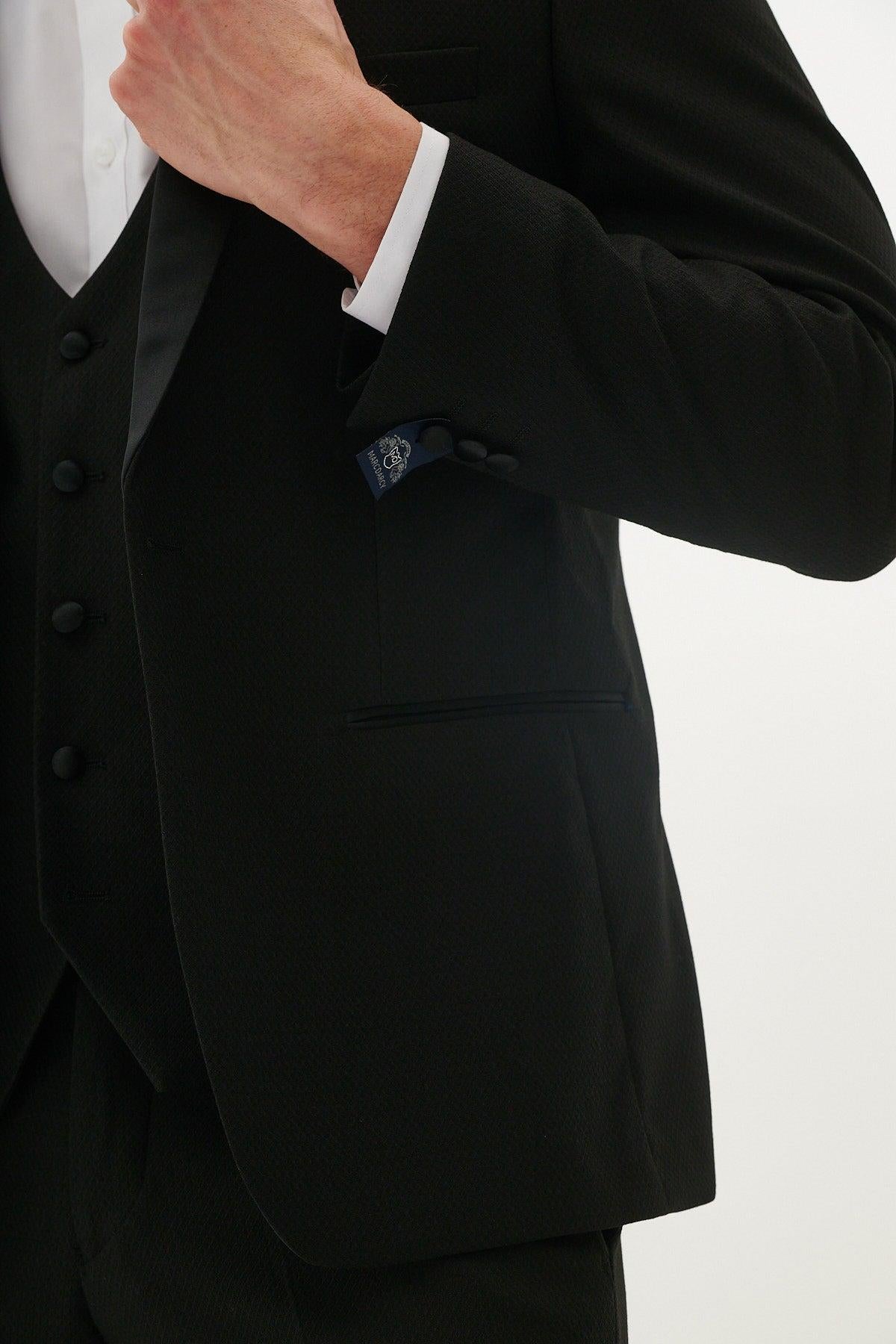 A person wearing the marcdarcy Matching Father & Son | DALTON Black Tux Three Piece Suit adjusts their jacket, revealing a pocket square and sleeve buttons. The image is cropped to show only the torso and a raised hand.