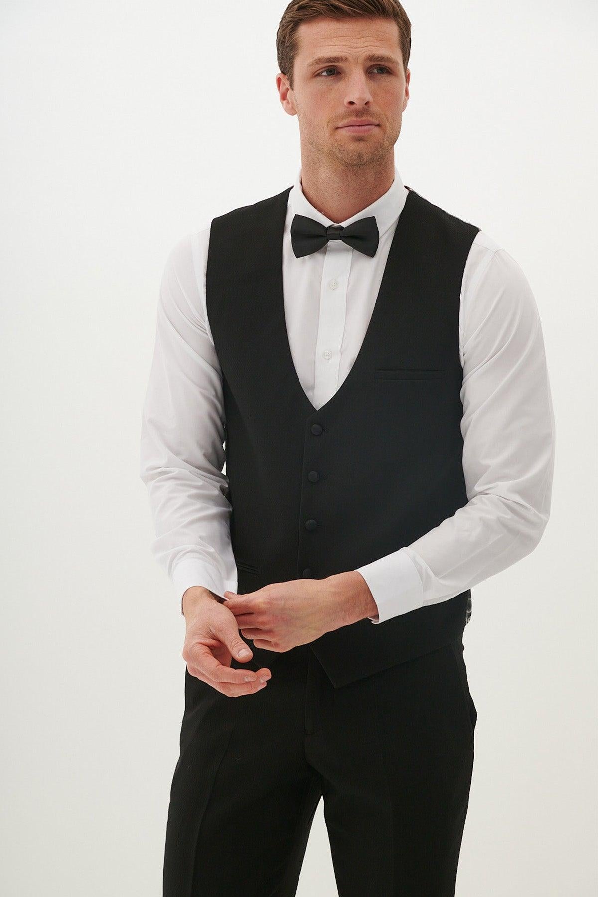 A man wearing the marcdarcy DALTON Black Tux Lapel Diamond Three Piece Suit with a white dress shirt and black bow tie adjusts his cuff links.