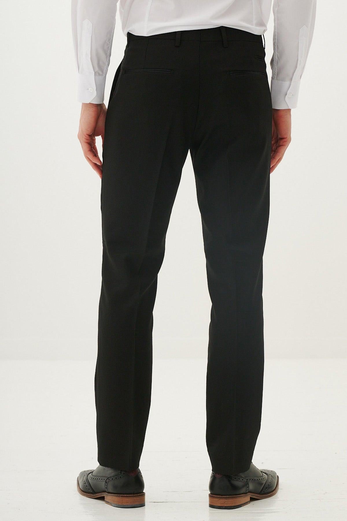 A man wearing the marcdarcy DALTON Black Tux Lapel Diamond Three Piece Suit stands with his back to the camera, showcasing the formal outfit paired with a white shirt and black trousers.