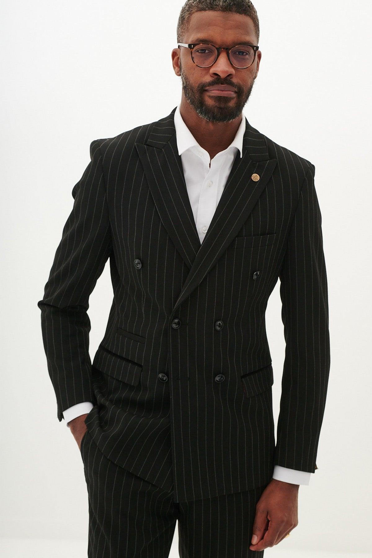 A Black man wears the Marc Darcy ROCCO Black Pinstripe Double Breasted Two Piece Suit with a white shirt, glasses, and a lapel pin.