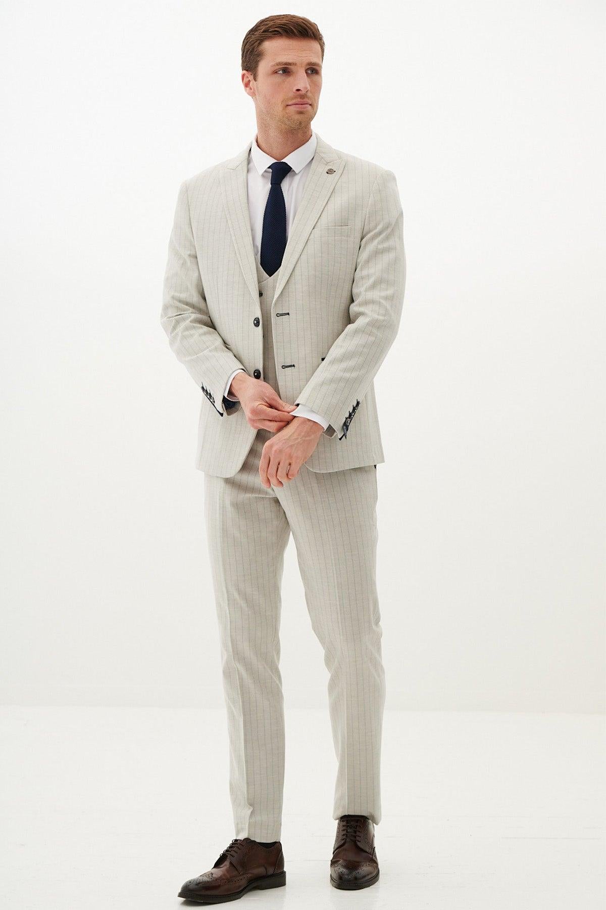 A man wears the Marc Darcy GRANT - Stone Pinstripe Three Piece Suit with a white shirt and dark tie, paired with brown dress shoes, posing against a plain white background.