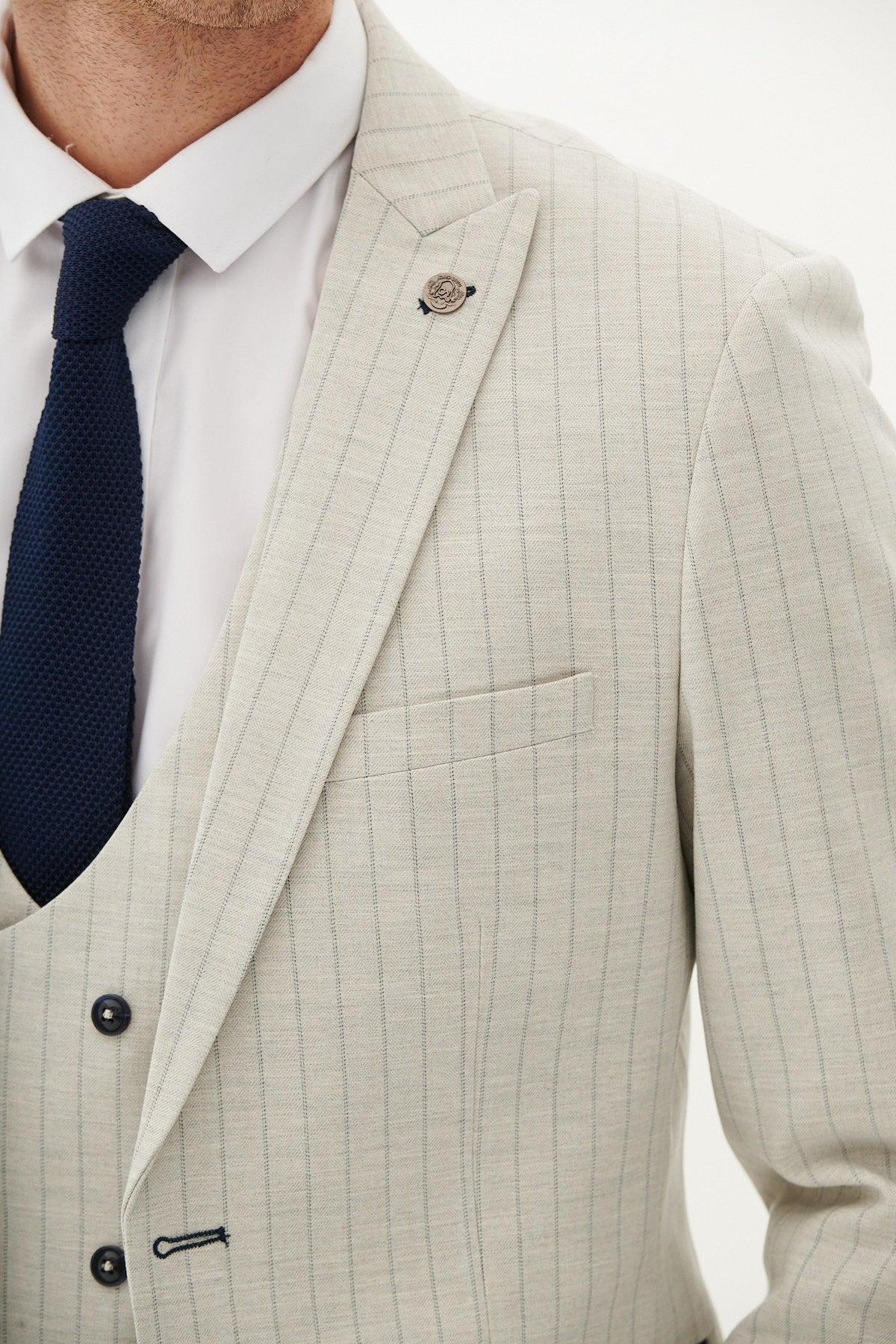 A close-up of a man wearing the Marc Darcy GRANT - Stone Pinstripe Blazer with a matching vest, white dress shirt, and dark navy textured tie. Only the upper torso is visible.
