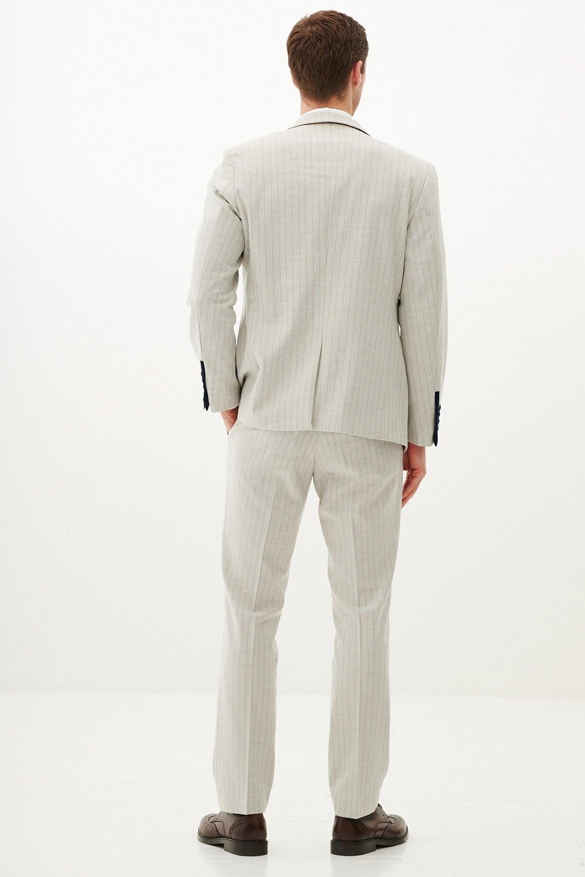 A man stands with his back to the camera, wearing the Marc Darcy GRANT Stone Pinstripe Three Piece Suit. One hand is in his pocket.