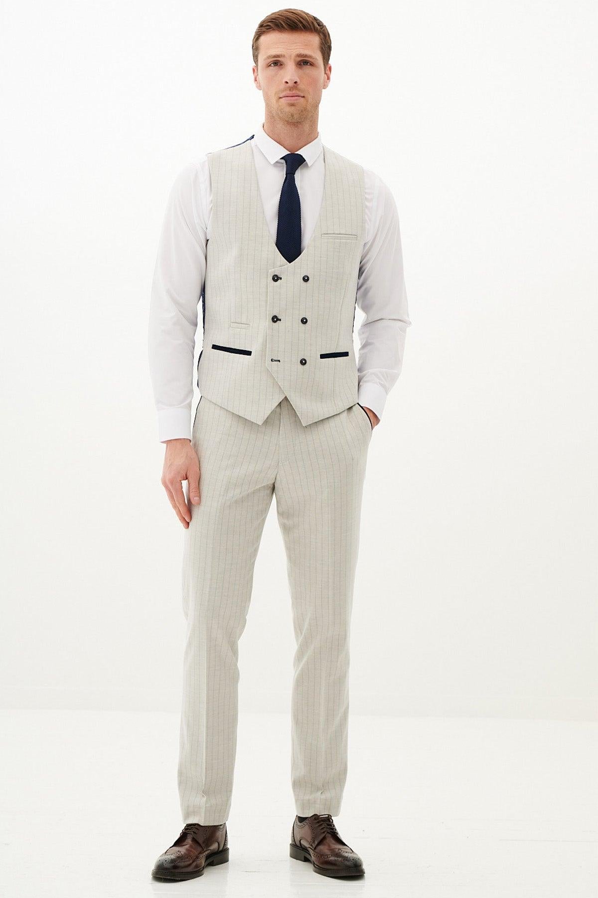 A man wears the Marc Darcy GRANT Stone Pinstripe Three Piece Suit, featuring a double-breasted vest, white shirt, and navy tie, posing against a white background.